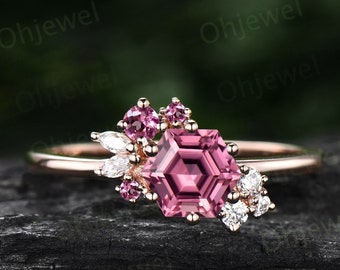 Puede incluir: Un anillo de oro rosa con una piedra preciosa rosa hexagonal rodeada de piedras preciosas rosas y blancas más pequeñas.
