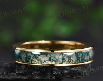 May include: A gold band ring with a green and white agate stone inlay. The ring is on a black surface.