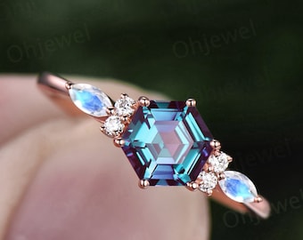Puede incluir: Un anillo de oro rosa con una piedra preciosa de alexandrita hexagonal rodeada de diamantes más pequeños y acentos de piedra lunar.