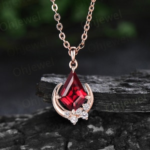 以下が含まれることがあります： 三日月型のペンダントに赤い宝石と小さな透明な宝石がついた、ローズゴールドのネックレスです。