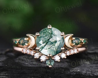 May include: A rose gold engagement ring set with a green moss agate gemstone and two crescent moon accents. The band is adorned with small diamonds and green gemstones.