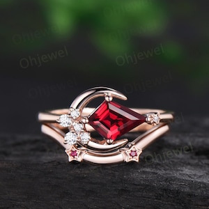 May include: Rose gold ring set featuring a kite-shaped, deep red gemstone, a crescent moon, and star accents. The ring is adorned with small, sparkling white gemstones. A matching band with star details completes the set, perfect for a celestial-themed jewelry collection.