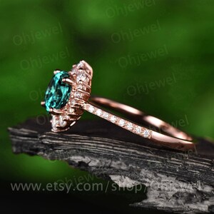 May include: A rose gold engagement ring with a large oval green gemstone surrounded by smaller round white gemstones. The ring has a band that is also set with smaller round white gemstones.