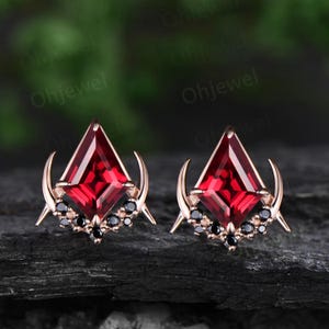 May include: A pair of rose gold earrings with a red gemstone and black diamonds. The earrings feature a crescent moon design.