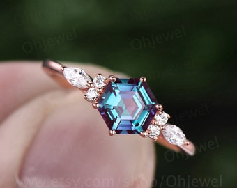 Könnte beinhalten: Ein Ring aus Roségold mit einem sechseckigen Alexandrit-Edelstein, der von kleineren Diamanten umgeben ist. Der Ring hat ein zartes Design mit Marquise-förmigen Diamanten auf beiden Seiten des Mittelsteins.