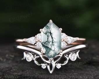 May include: A rose gold engagement ring set with a moss agate center stone and a delicate, ornate band. The moss agate is a unique green and white stone with a natural, organic pattern.