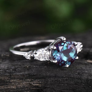 Pode incluir: Um anel de prata com uma grande gema redonda azul-esverdeada cercada por gemas menores em forma de p&ecirc;ra transparentes.