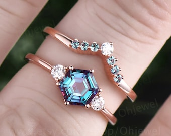 May include: A rose gold ring set with a hexagonal alexandrite gemstone surrounded by smaller white diamonds. The ring is paired with a matching rose gold band featuring a row of smaller alexandrite gemstones and a larger white diamond.