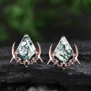 May include: A pair of rose gold earrings featuring a green and white dendritic agate gemstone in a diamond shape, surrounded by black onyx stones and crescent moon accents.