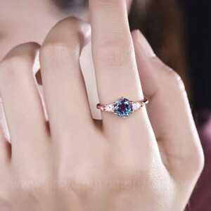 Pode incluir: Um anel de ouro rosa com uma gema redonda azul-esverdeada cercada por tr&ecirc;s gemas brancas menores em forma de p&ecirc;ra.