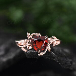 May include: A rose gold ring with a heart-shaped red garnet gemstone surrounded by a delicate vine design with small diamonds.