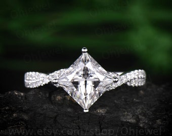 May include: A silver engagement ring with a square princess-cut diamond center stone and a twisted band accented with smaller diamonds.