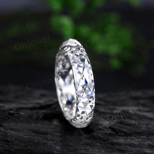 May include: A clear, faceted ring with a brilliant cut, showcasing a multitude of reflective surfaces. The ring is set against a dark, textured background, highlighting its sparkle and intricate design. The ring appears to be made of a clear gemstone.