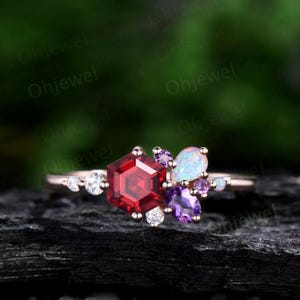 May include: A rose gold ring with a hexagonal red gemstone surrounded by smaller white, purple, and opal gemstones.