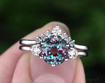 May include: A silver ring set with a large, round, iridescent alexandrite gemstone surrounded by smaller white and blue gemstones. The ring is set on a silver band.