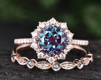 May include: A rose gold engagement ring set with a large, round, iridescent alexandrite center stone surrounded by a halo of smaller diamonds. The matching wedding band features a delicate design with alexandrite accents.