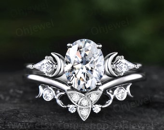 Könnte beinhalten: Ein silberner Ring mit einem großen ovalen Diamanten, umgeben von einem zarten Halbmond-Design. Die Band verfügt über ein keltisches Knotendesign mit kleineren Diamanten.