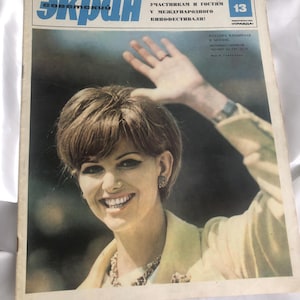May include: A vintage magazine cover featuring a smiling woman with short brown hair, wearing a light yellow jacket and a necklace. The magazine title is in blue Cyrillic script, with additional text in Russian. The year 1967 is visible.