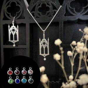 May include: Silver-toned gothic-style pendant necklace and matching earring set. The pendant and earrings feature a cathedral window design with a dangling clear crystal. A selection of colorful crystal charms are also shown.