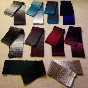 May include: A collection of 10 crocheted scarves in various colors, including black, gray, blue, green, red, and white. The scarves are arranged in two rows on a beige surface.