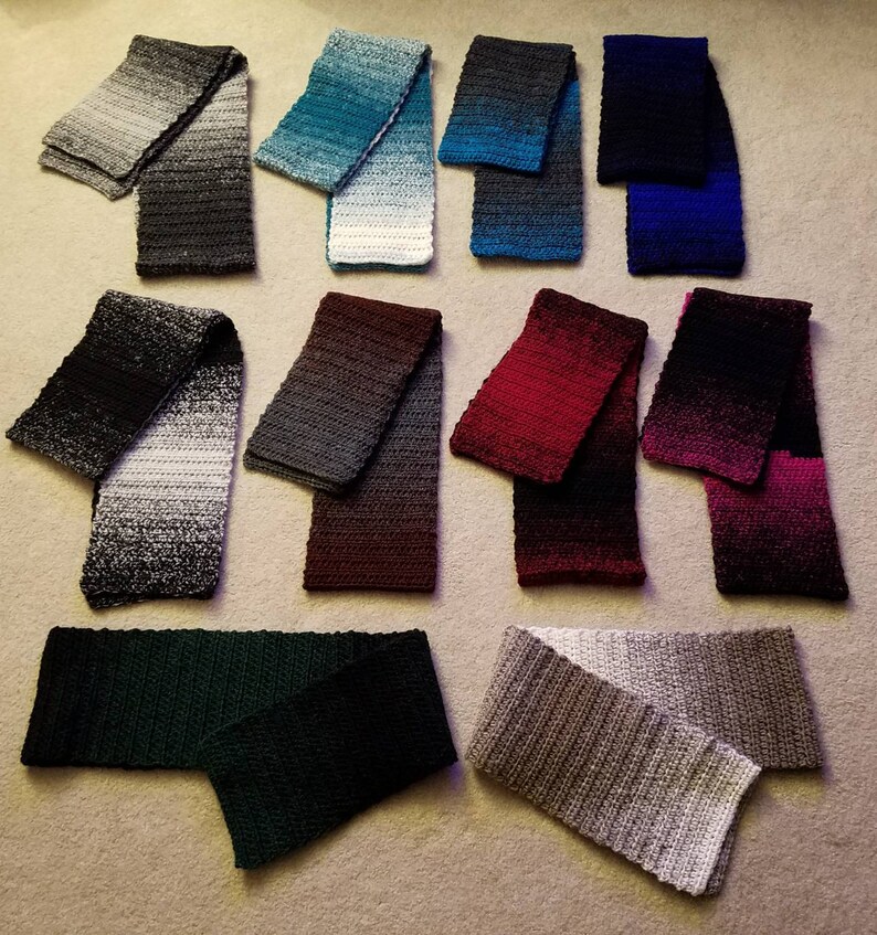 May include: A collection of 10 crocheted scarves in various colors, including black, gray, blue, green, red, and white. The scarves are arranged in two rows on a beige surface.