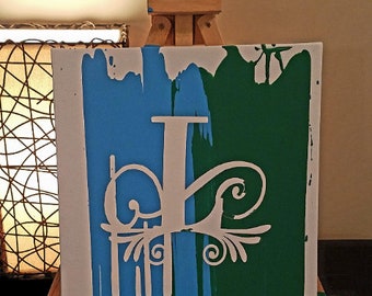 May include: A white canvas with blue and green paint strokes. A white stencil of a stylized letter "P" with a decorative flourish is on the canvas. The canvas is on an easel.