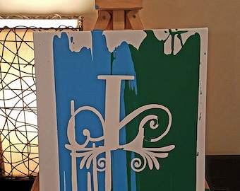 May include: A white canvas with a blue and green background. The canvas has a white stencil of the letter "P" with a decorative flourish. The canvas is on an easel.