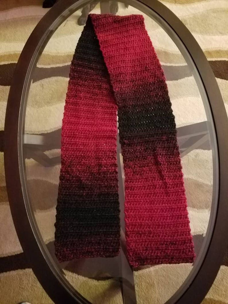 May include: A red and black ombre crochet scarf. The scarf is made with a soft yarn and has a subtle shimmer.