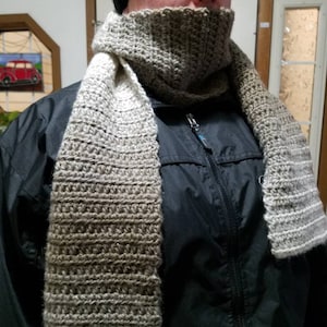 May include: A brown and beige crocheted scarf with a matching crocheted cowl. The scarf is worn by a person wearing a black jacket.