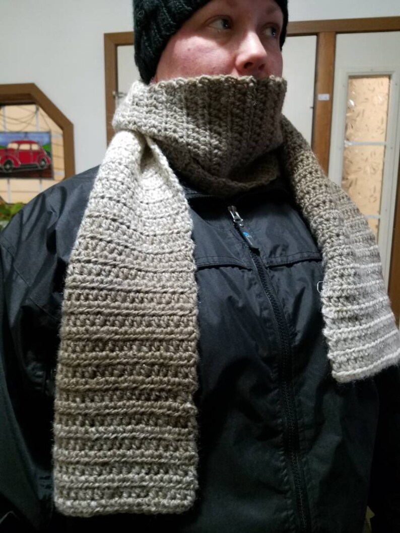 May include: A brown and beige crocheted scarf with a matching crocheted cowl. The scarf is worn by a person wearing a black jacket.