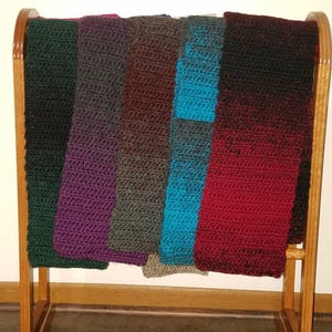 May include: A wooden rack with seven crocheted scarves in various colors, including green, purple, brown, teal, and red.