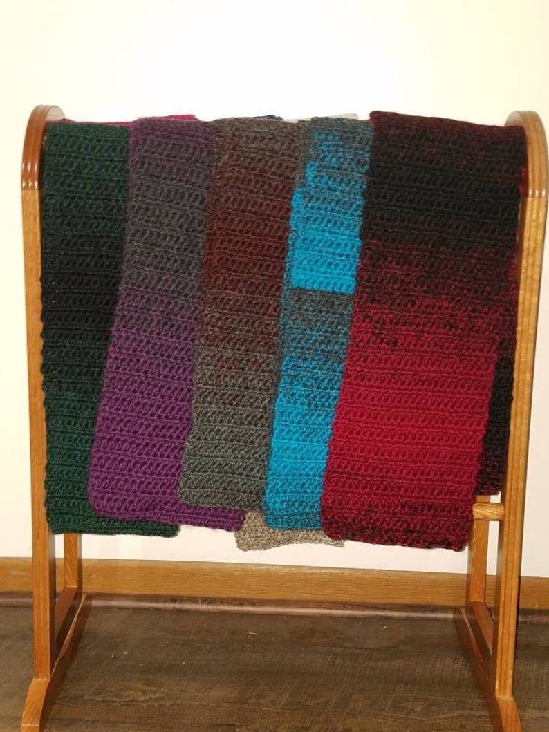 May include: A wooden rack with seven crocheted scarves in various colors, including green, purple, brown, teal, and red.