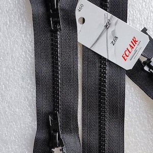 May include: Close-up of a black zipper with a metal pull. A white tag with the text "ECLAIR" and "Z68" is attached. The zipper teeth are visible, and the overall design is sleek and functional.