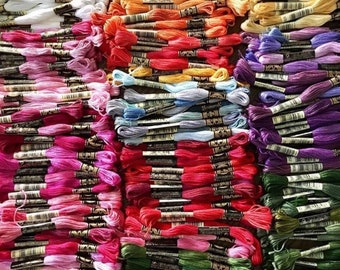 May include: A large collection of embroidery floss spools in various colors, including white, pink, red, orange, yellow, green, blue, purple, and black. The spools are arranged in rows and columns, creating a colorful and organized display.