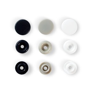 May include: Nine snap fasteners arranged in a grid. The top row shows three flat, solid snaps in navy, grey, and white. The middle and bottom rows display the snap components, with a central hole, in matching colours.
