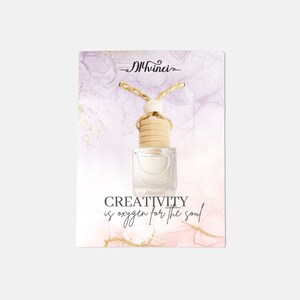 May include: Clear glass car air freshener with a wooden cap and a decorative cord. The card behind the freshener has a watercolor design in shades of purple and pink, with the text "CREATIVITY is oxygen for the soul."