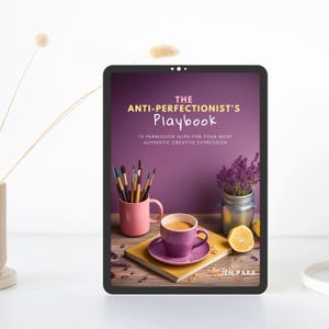 以下が含まれることがあります： 「THE ANTI-PERFECTIONIST'S Playbook」というタイトルと「12 PERMISSION SLIPS FOR YOUR MOST AUTHENTIC CREATIVE EXPRESSION」というサブタイトルが書かれた本の表紙が表示されたデジタルタブレット。表紙は紫色の背景に、コーヒーカップ、ラベンダーの瓶、筆立てが描かれている。