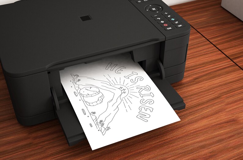 May include: A black and white printable coloring page featuring a mountain with a sun and the text "He is Risen". The page is being printed from a black printer.
