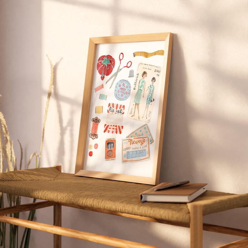 May include: A framed illustration of vintage sewing supplies, including spools of thread, buttons, scissors, a thimble, a tape measure, and a pattern for a dress. The illustration is in a watercolor style and features a red, white, and blue color scheme.