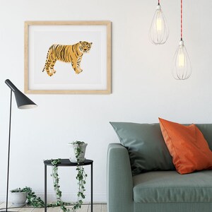 May include: A living room interior with a green sofa, two orange throw pillows, a black side table with a potted plant, a framed print of a tiger, and two hanging pendant lights with red cords.
