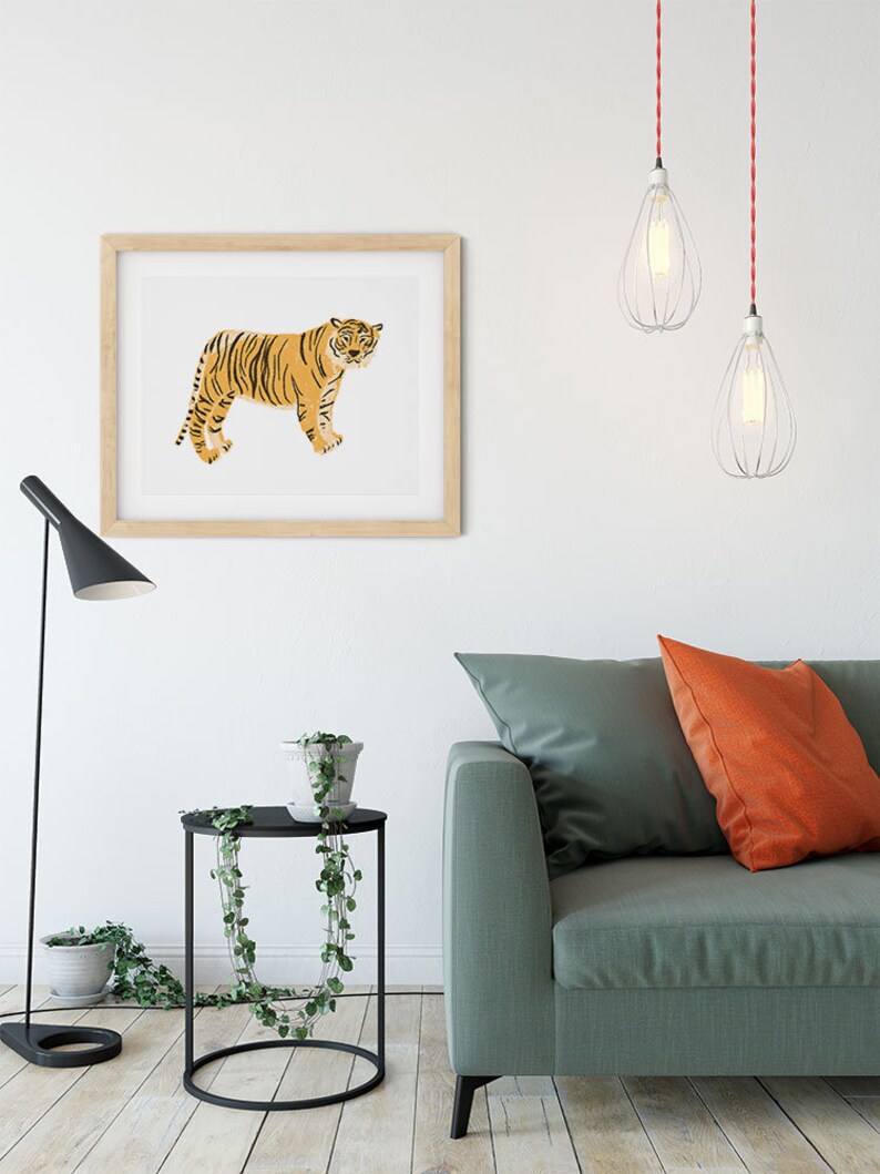 May include: A living room interior with a green sofa, two orange throw pillows, a black side table with a potted plant, a framed print of a tiger, and two hanging pendant lights with red cords.