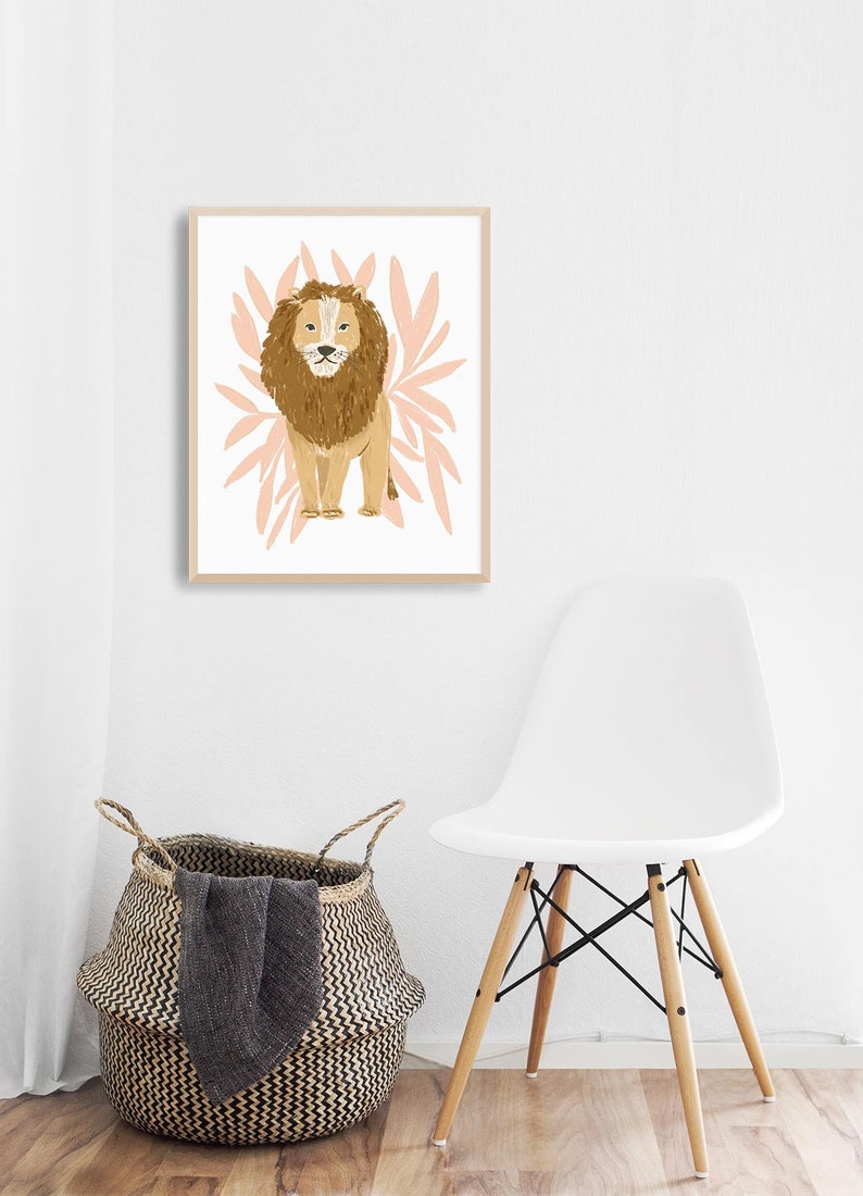 May include: A framed art print featuring a lion illustration. The lion is depicted in shades of brown and tan, set against a backdrop of pink leaf-like shapes. The artwork is in a light wooden frame, suitable for nursery or home decor.