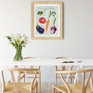 May include: A framed print with a light blue background and the word "Vegetables" written in black cursive. The print features illustrations of various vegetables, including a tomato, carrot, broccoli, eggplant, onion, and peas.