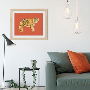 May include: A framed print of a tiger on a red background. The print is hanging on a white wall above a green sofa with orange throw pillows. There is a black side table with a potted plant next to the sofa.