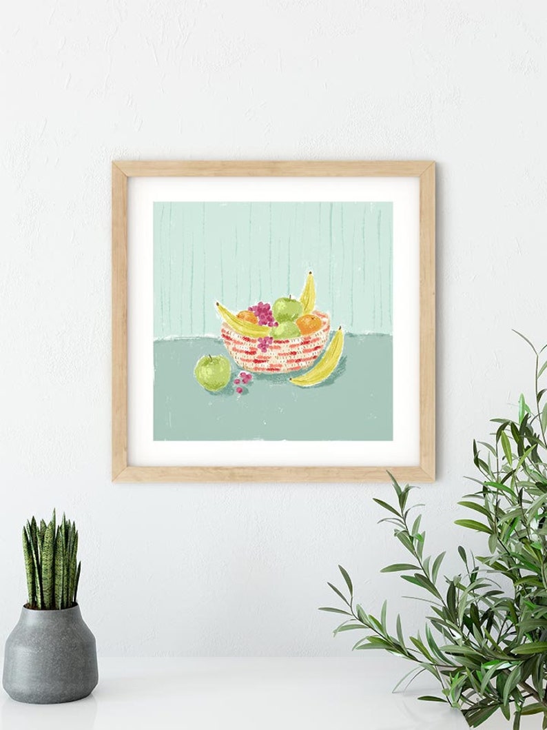 May include: A framed illustration of a bowl of fruit. The bowl is red and white striped and contains bananas, apples, and grapes. The bowl is sitting on a light blue surface with a striped pattern.