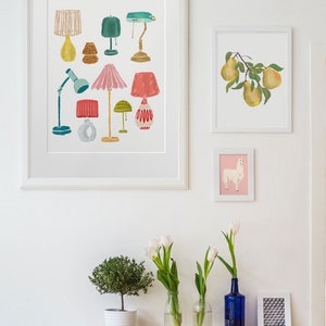 K&ouml;nnte beinhalten: Ein wei&szlig;er gerahmter Druck mit einer Sammlung von bunten Lampen in verschiedenen Stilen und Designs. Der Druck h&auml;ngt an einer wei&szlig;en Wand mit anderen gerahmten Drucken und einem Holztisch mit Pflanzen und Vasen.