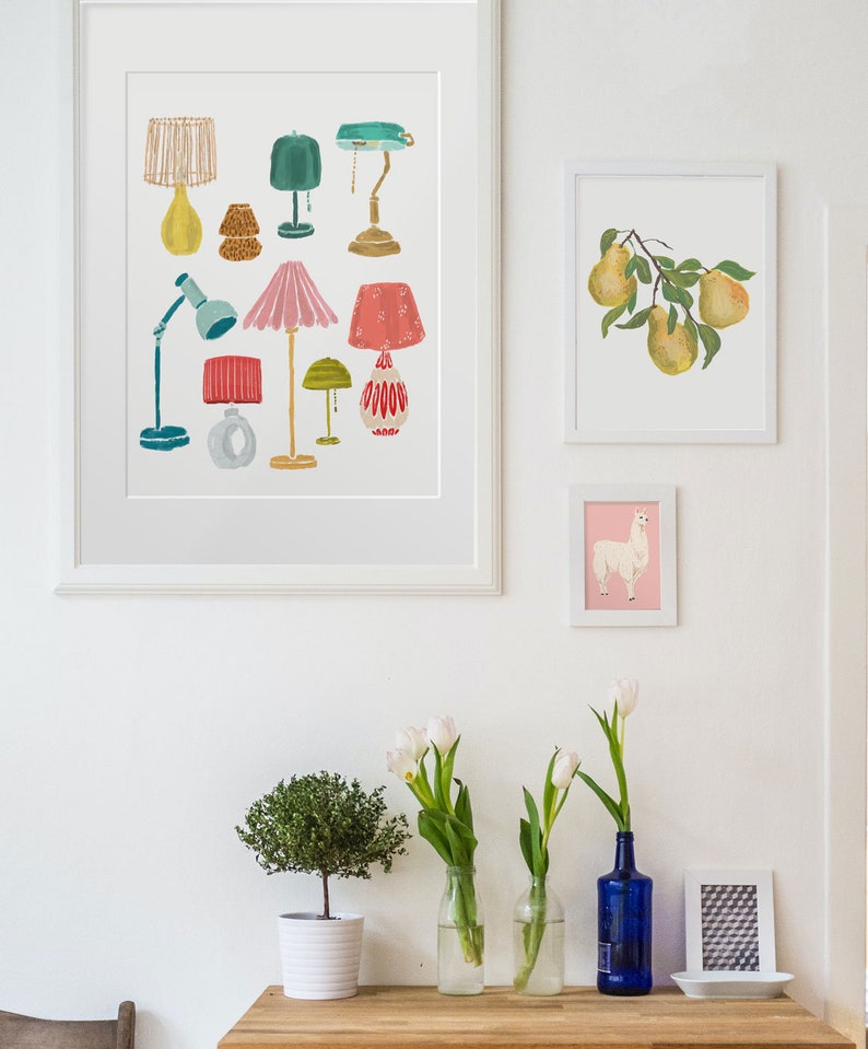 K&ouml;nnte beinhalten: Ein wei&szlig;er gerahmter Druck mit einer Sammlung von bunten Lampen in verschiedenen Stilen und Designs. Der Druck h&auml;ngt an einer wei&szlig;en Wand mit anderen gerahmten Drucken und einem Holztisch mit Pflanzen und Vasen.