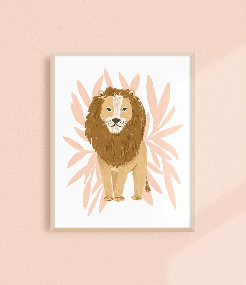 May include: A framed art print featuring a stylized illustration of a lion. The lion has a brown mane and body, with a white face and chest. The background includes pink leaf-like shapes, and the frame is a light beige color.