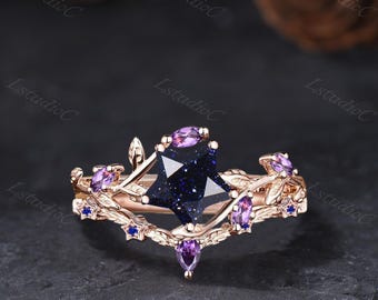 Könnte beinhalten: Ein Ring aus Roségold mit einem sternförmigen, dunkelblauen Sandstein in der Mitte, akzentuiert durch violette Edelsteine im Marquise-Schliff und kleine sternförmige Details. Die Ringschiene hat eine rankenartige Textur mit weiteren violetten Steinen.