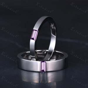 May include: Two silver wedding bands with a single purple gemstone on each band.